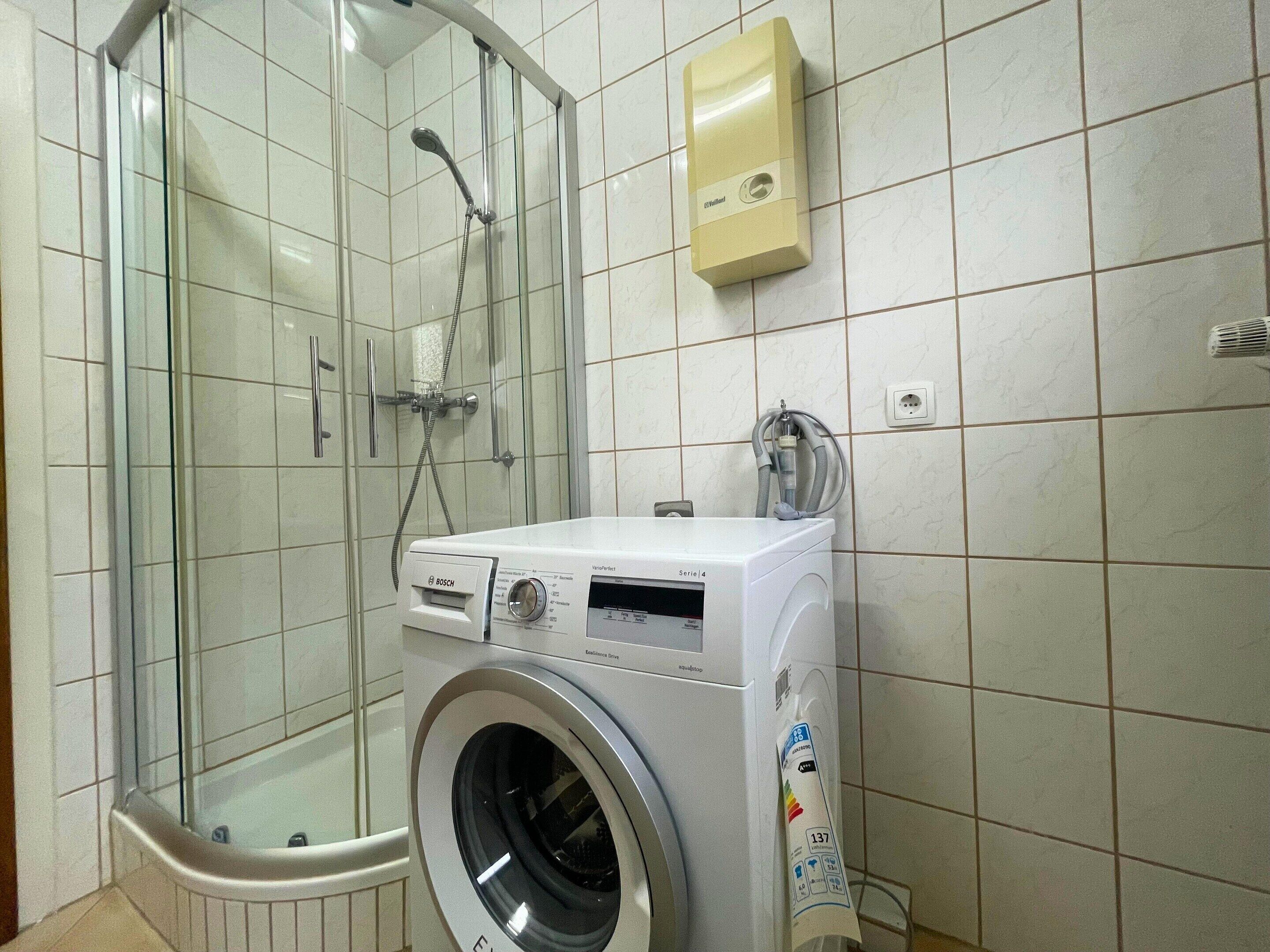 A bathroom with a glass-enclosed shower, a Bosch washing machine, and a hand dryer.
