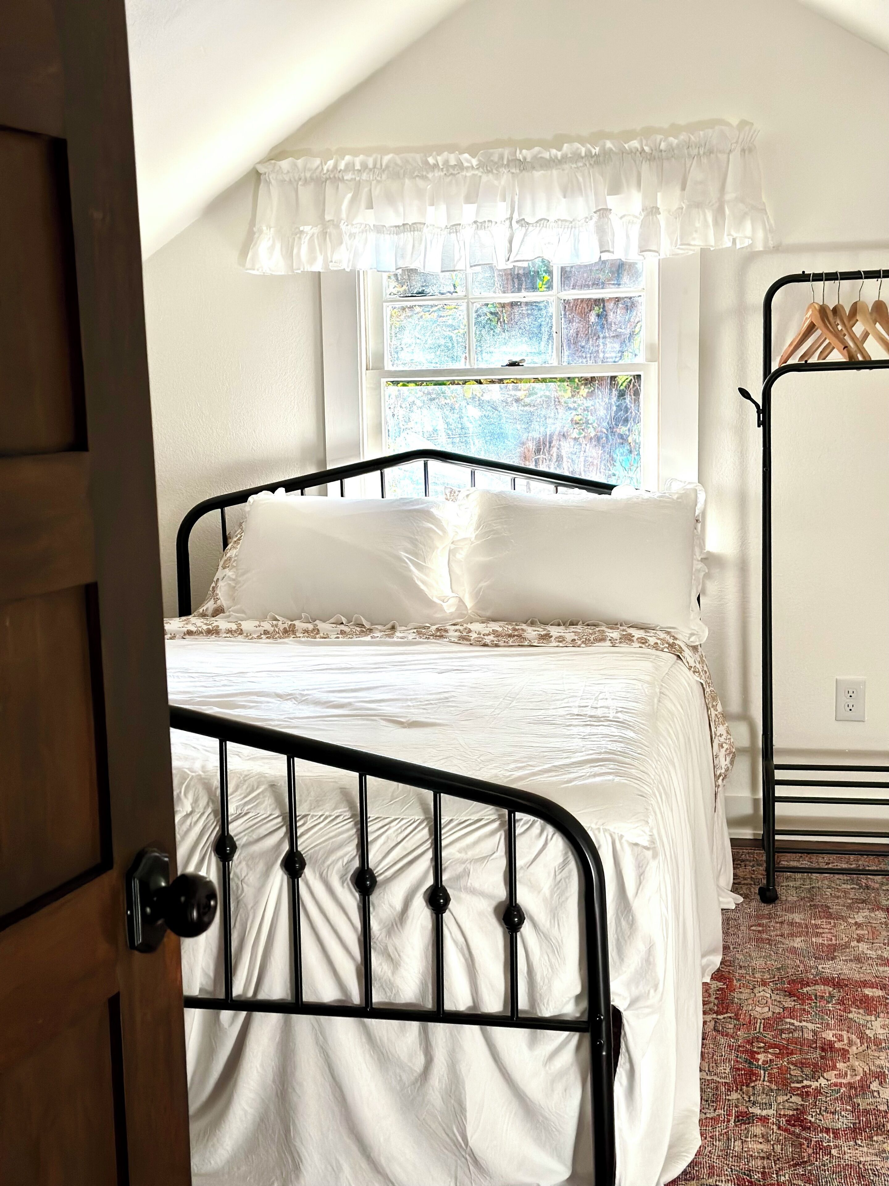 A bedroom with a bed, a window with curtains, a radiator, and a door.