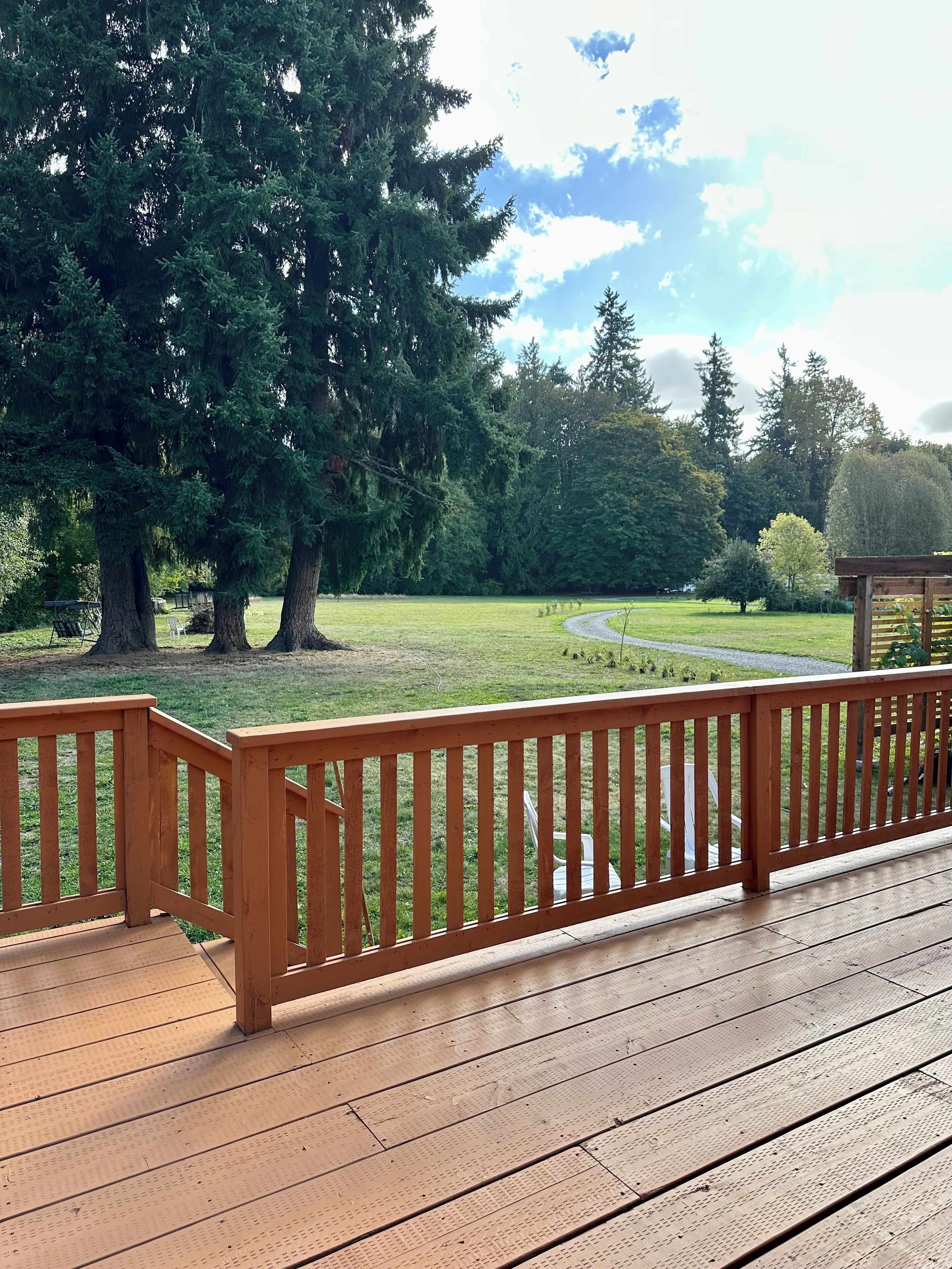 A wooden deck with a railing overlooking a grassy area with trees and a clear sky.