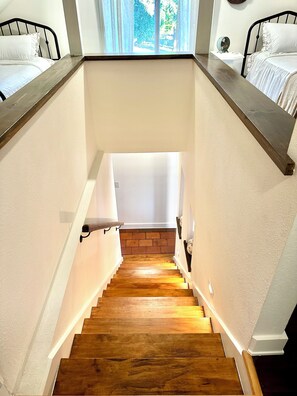 A wooden staircase with a brick wall at the bottom, white walls, and a window with curtains.