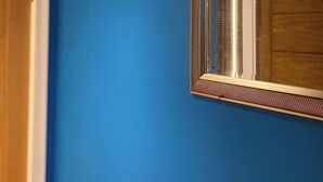 Una habitación con una pared azul, una puerta de madera y un espejo con un marco texturizado.