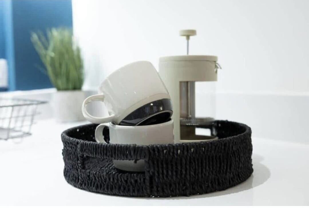 A white coffee maker on a white countertop with a black woven tray underneath.