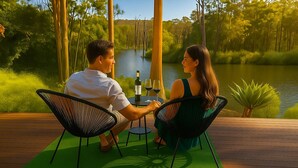 Una coppia seduta a un tavolo con una bottiglia di vino e due bicchieri, con vista su un corpo d'acqua e alberi sullo sfondo.