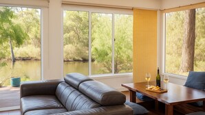 Un soggiorno moderno con un divano in pelle, un tavolo da pranzo in legno con bicchieri da vino e ampie finestre che si affacciano su un paesaggio naturale.