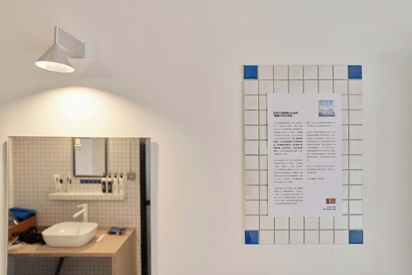 A bathroom with a sink, mirror, and a wall-mounted light fixture. There is a notice taped to the wall. - Tiaohai Living Youth Hotel (Shenzhen)