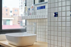 A bathroom with a white sink, a window, and a tiled wall with a blue accent. - Tiaohai Living Youth Hotel (Shenzhen)