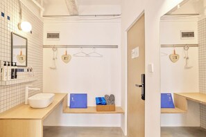 A modern bathroom with a white sink, mirror, and towel rack. There are shelves with toiletries and a blue storage box. - Tiaohai Living Youth Hotel (Shenzhen)
