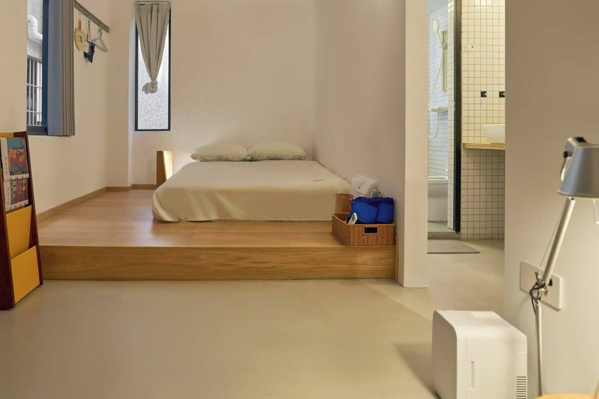 A bedroom with a bed, a bedside table, a lamp, and a view of the bathroom.