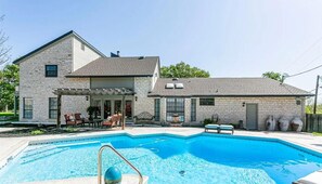 Ein zweistöckiges Haus mit Schwimmbad, Gartenmöbeln und einer Pergola.