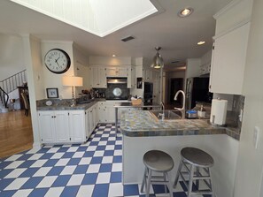 A modern kitchen with white cabinets, a blue and white checkered floor, a large clock, and a skylight. - Haven Getaway (Belton)