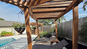 Eine hölzerne Pergola mit hängendem Blumentopf und einem Poolbereich mit Liegestühlen.