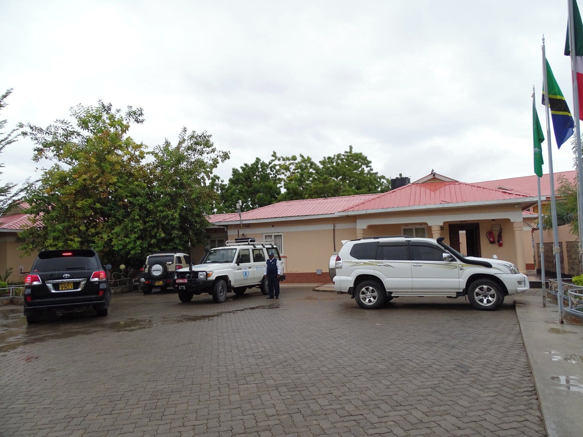 A building with a red roof, a paved driveway, and several vehicles parked in front.