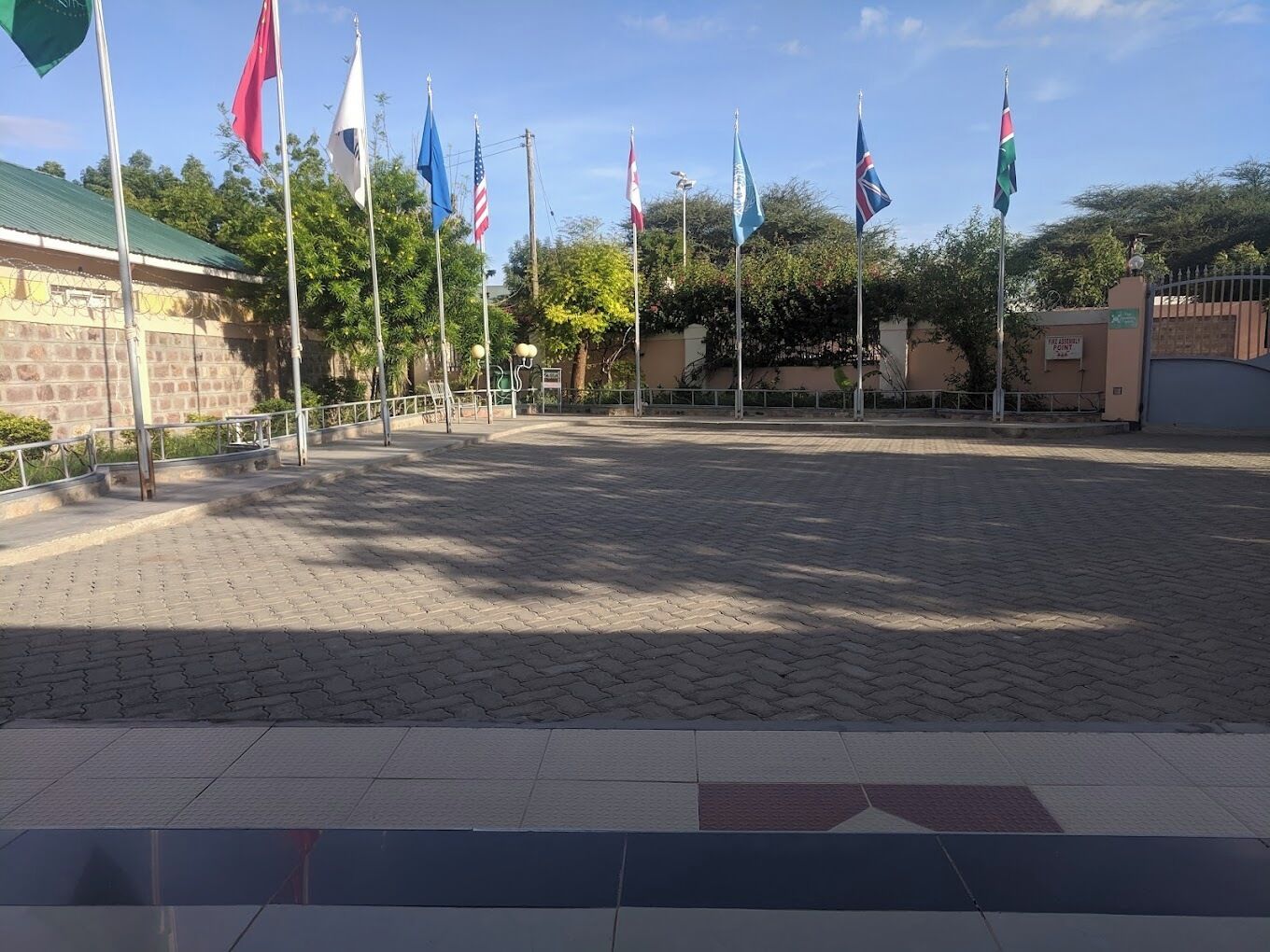 A paved plaza with multiple flags, a building with a green roof, and a gated entrance.