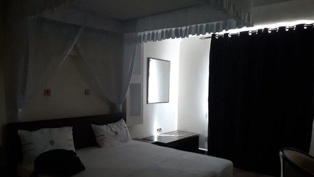 Quarto de hotel com uma cama grande, mesa de cabeceira, uma cadeira e janela com cortinas.