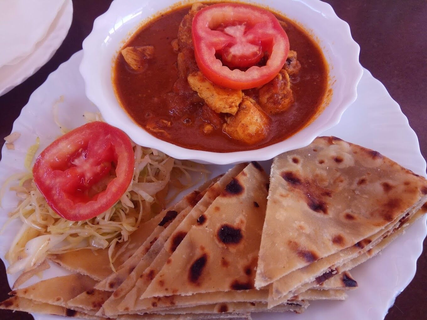 A plate with a curry dish, flatbread, and a side of shredded cabbage.