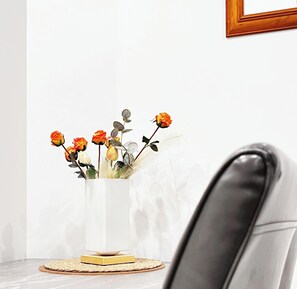 A white vase with flowers on a table, a framed picture on the wall, and a black chair. - Free Parking & A/C Cooling & CBD View (Wellington)