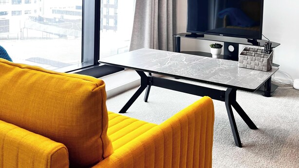 Une chambre d’hôtel moderne dotée d’une grande fenêtre, d’un téléviseur à écran plat, d’une petite table et d’un fauteuil jaune.