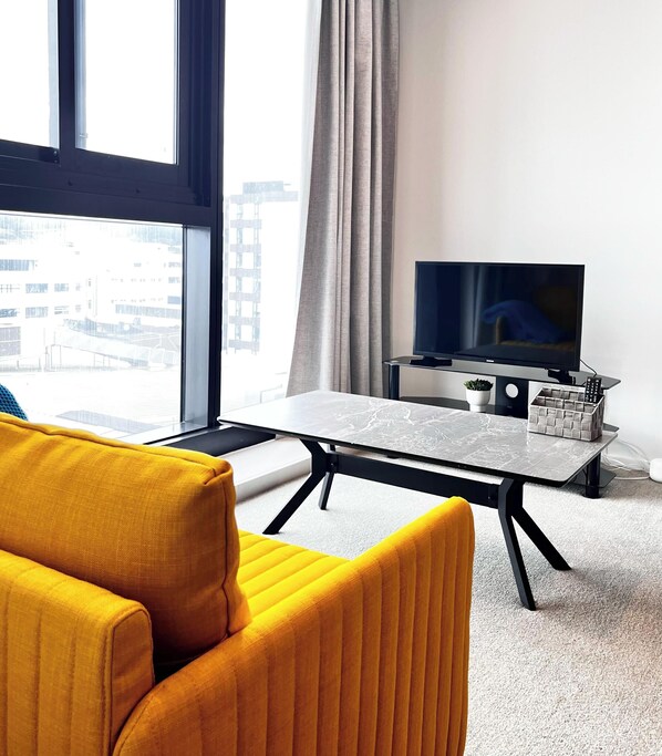 A modern hotel room with a large window, a flat-screen TV, a small table, and a yellow armchair. - Free Parking & A/C Cooling & CBD View (Wellington)