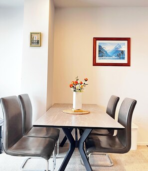 A dining area with a marble table, black leather chairs, a vase of flowers, and two framed pictures on the wall. - Free Parking & A/C Cooling & CBD View (Wellington)