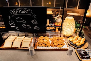 A bakery display with various pastries and bread, a chalkboard sign, and a decorative lamp.