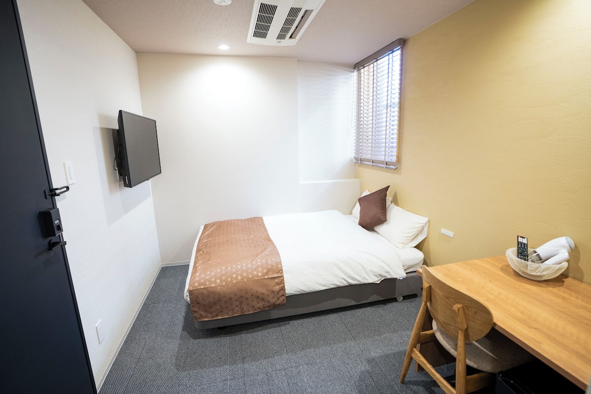 Quarto de hotel pequeno e bem organizado, com uma cama, escrivaninha e televisão.