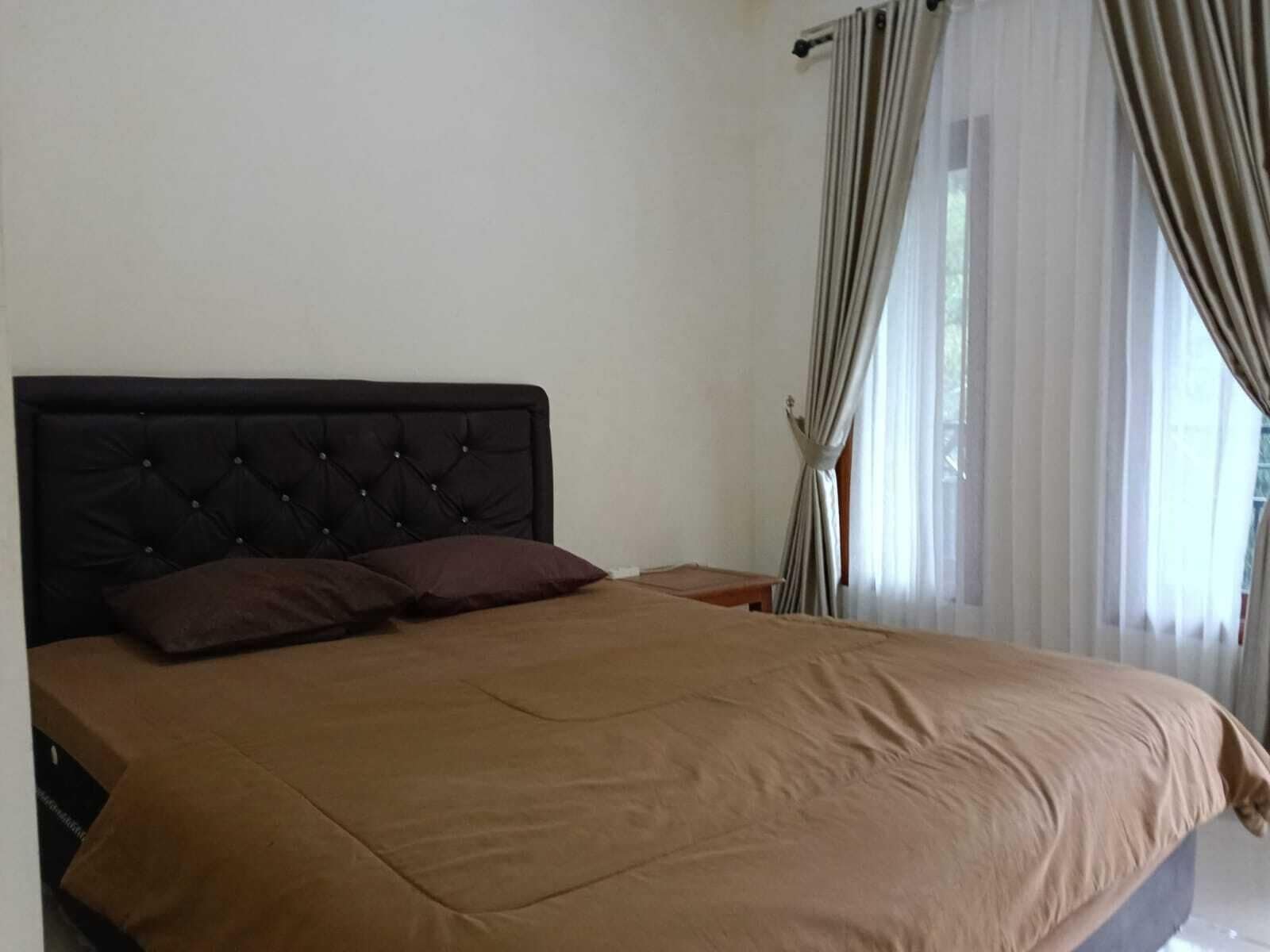 A bedroom with a large bed, a nightstand, and a window with curtains.