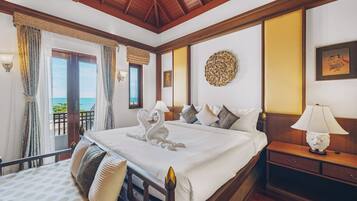 Habitación de hotel con una cama grande, una mesita de noche, una lámpara, un adorno de pared y vista al mar desde un balcón.