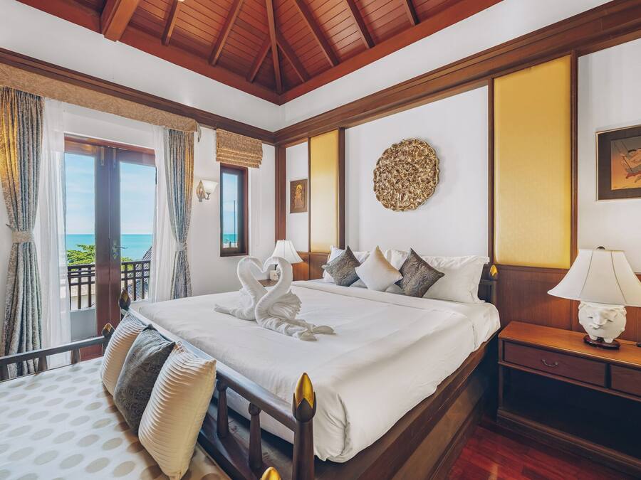 Habitación de hotel con una cama grande, una mesita de noche, una lámpara, un adorno de pared y vista al mar desde un balcón.