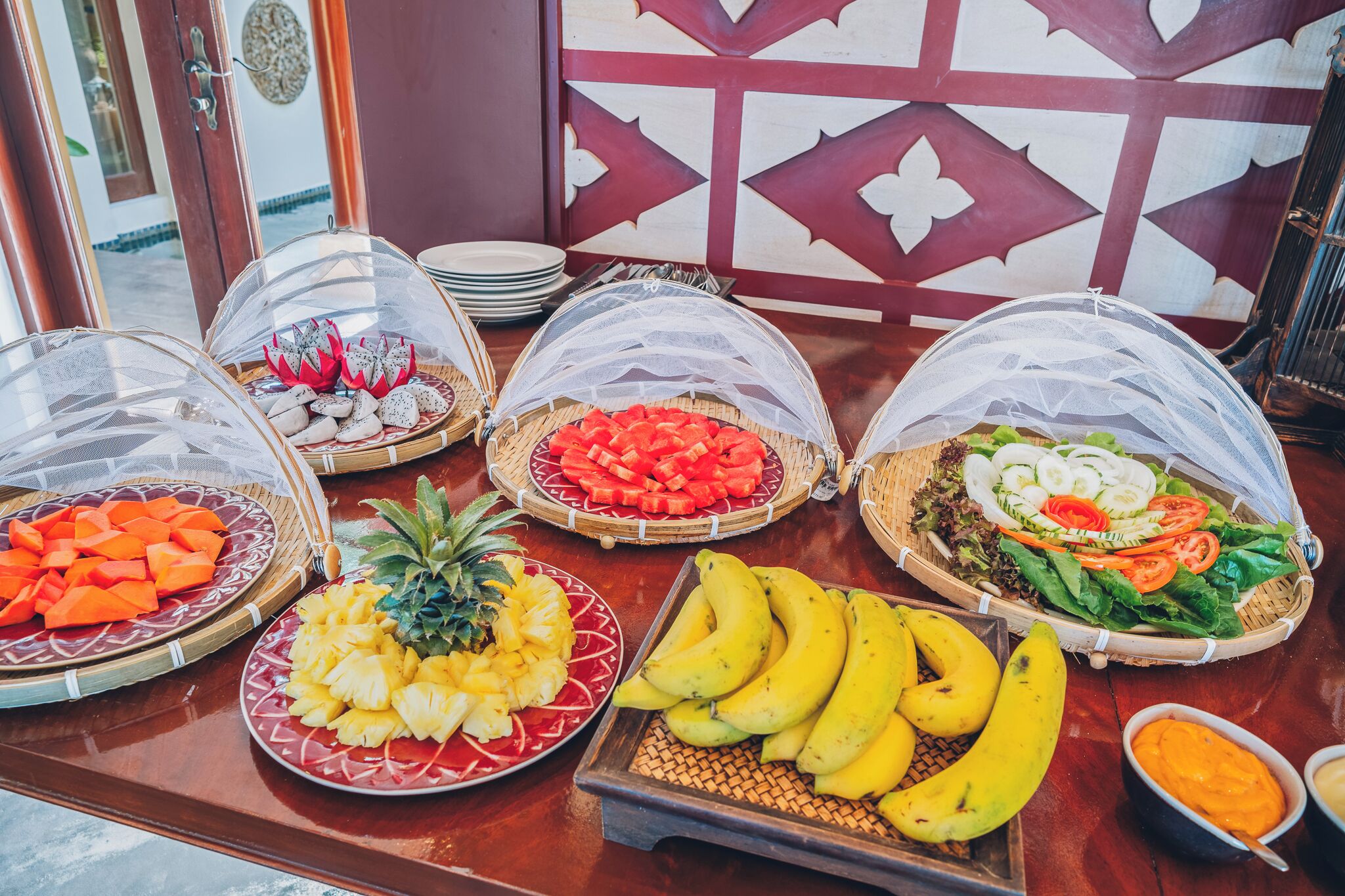 Une table de buffet garnie de divers fruits et légumes, le tout recouvert d’un filet de protection.