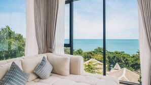 A modern living room with a large window overlooking a coastal view. - Leva Boutique Hotel (Koh Samui)