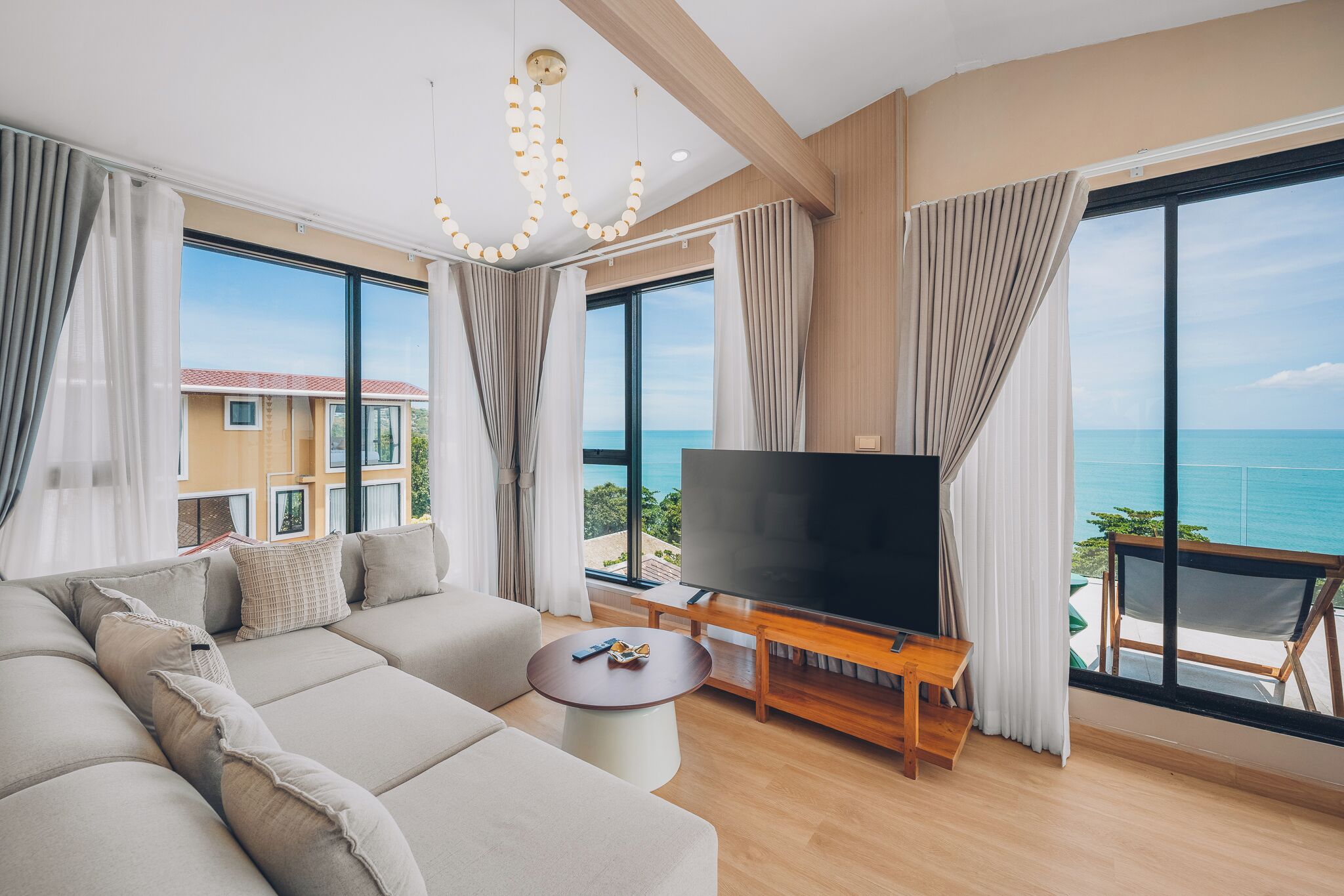 A modern living room with a large TV, beige sofa, and a view of the ocean.