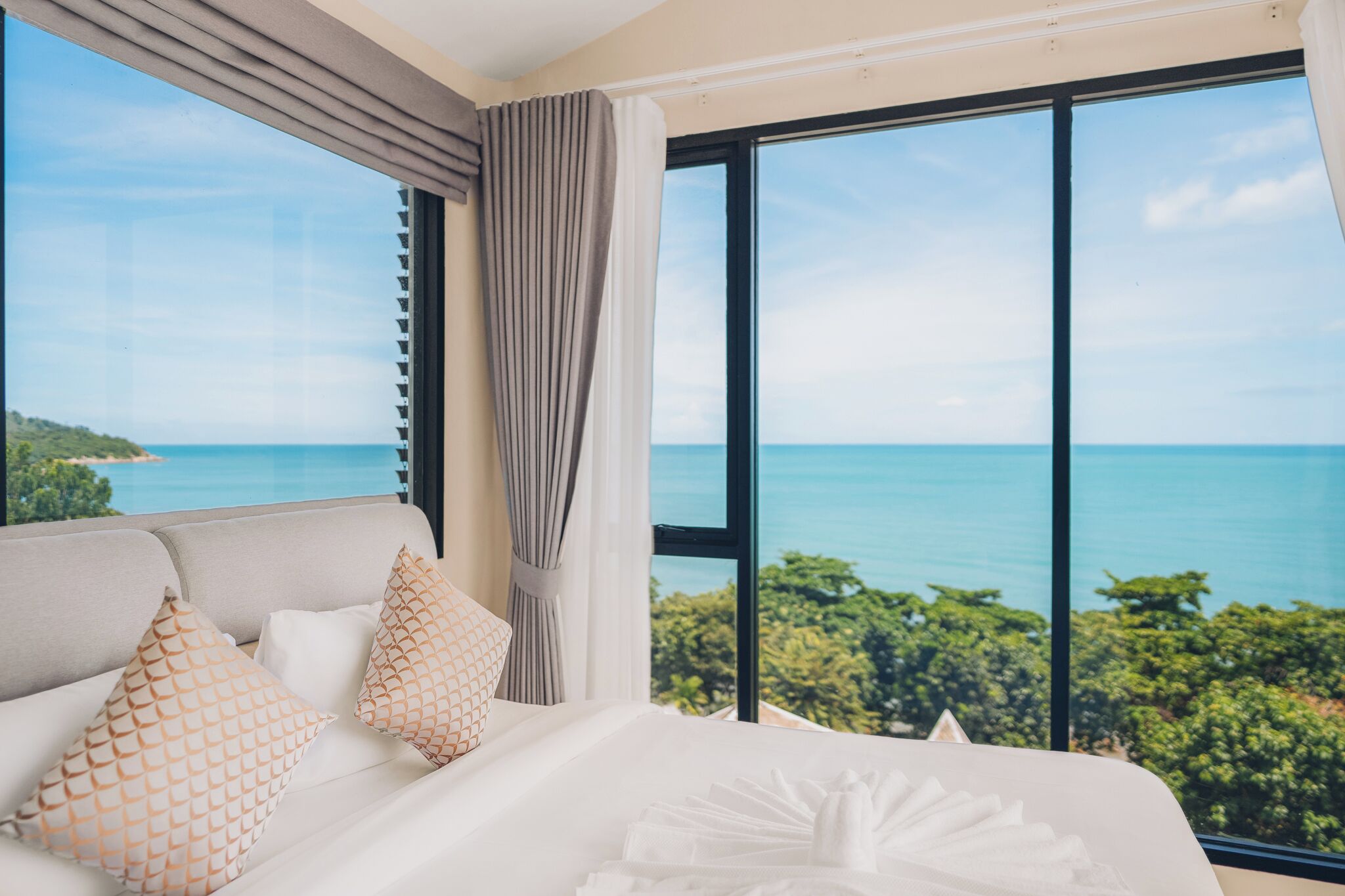 A bedroom with a large window offering a view of the sea and greenery.