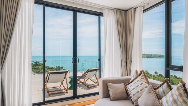 A balcony with a view of the sea, a sofa with patterned cushions, and a pair of wooden chairs. - Leva Boutique Hotel (Koh Samui)
