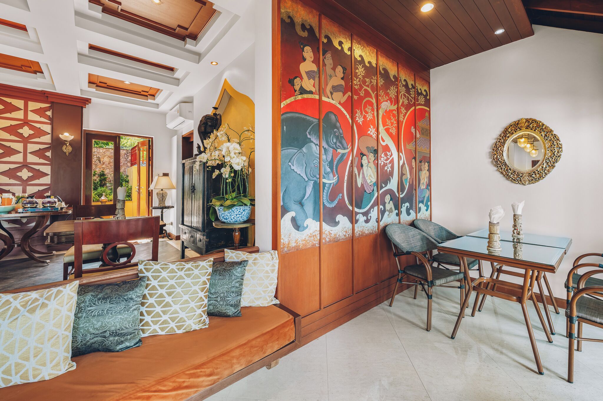 A traditional interior with a dining area, cushioned seating, and a decorative wall with cultural artwork.