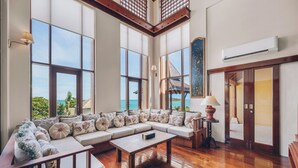 A spacious living room with a large sectional sofa, wooden flooring, and large windows offering a view of the sea. - Leva Boutique Hotel (Koh Samui)