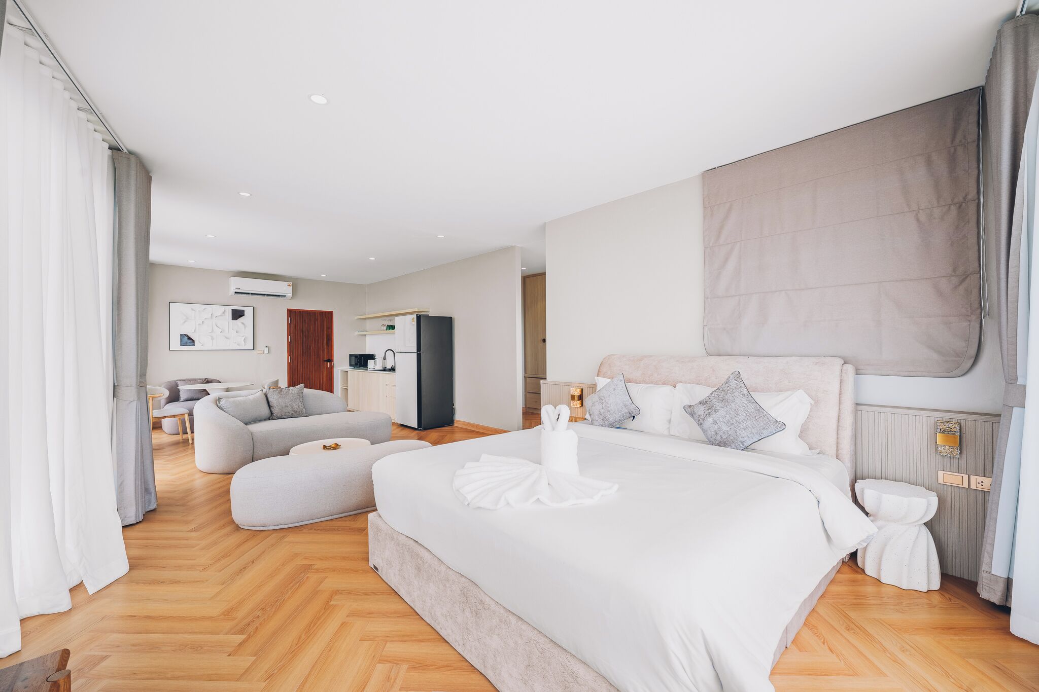 Une chambre d’hôtel moderne équipée d’un grand lit, d’un canapé, d’une petite table et d’une kitchenette.