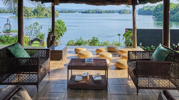 A covered outdoor seating area with wicker furniture and a view of a lake.
