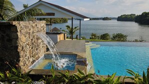A pool with a waterfall feature, a stone wall, and a view of a lake and distant mountains.