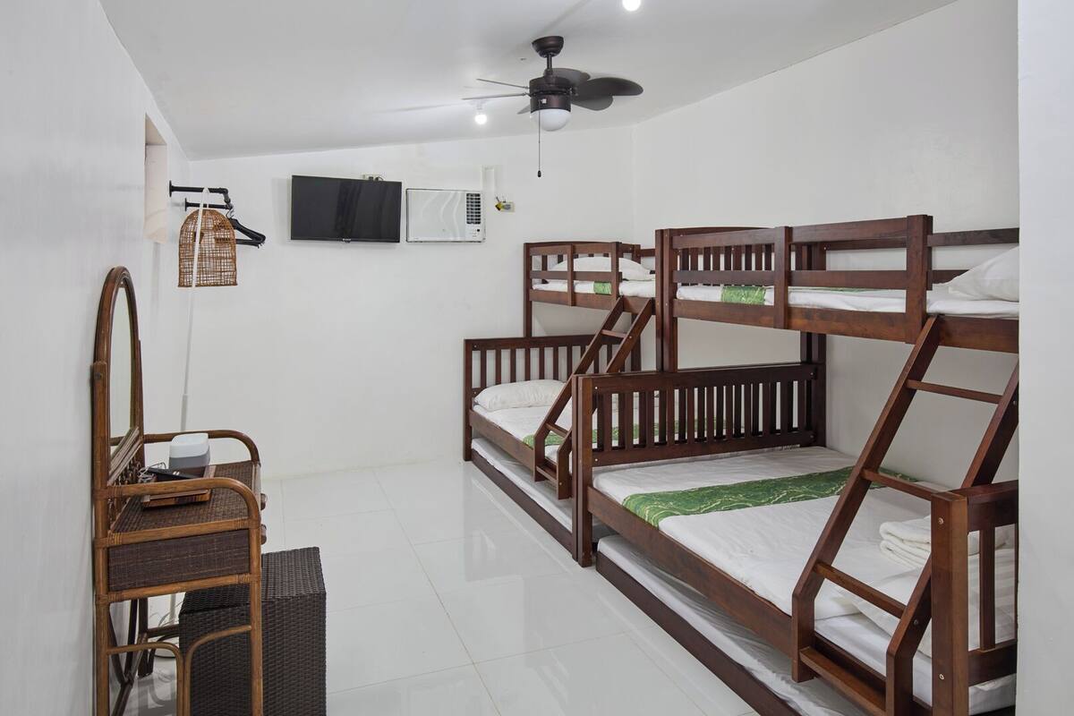 A dormitory room with bunk beds, a television, an air conditioning unit, and a ceiling fan.