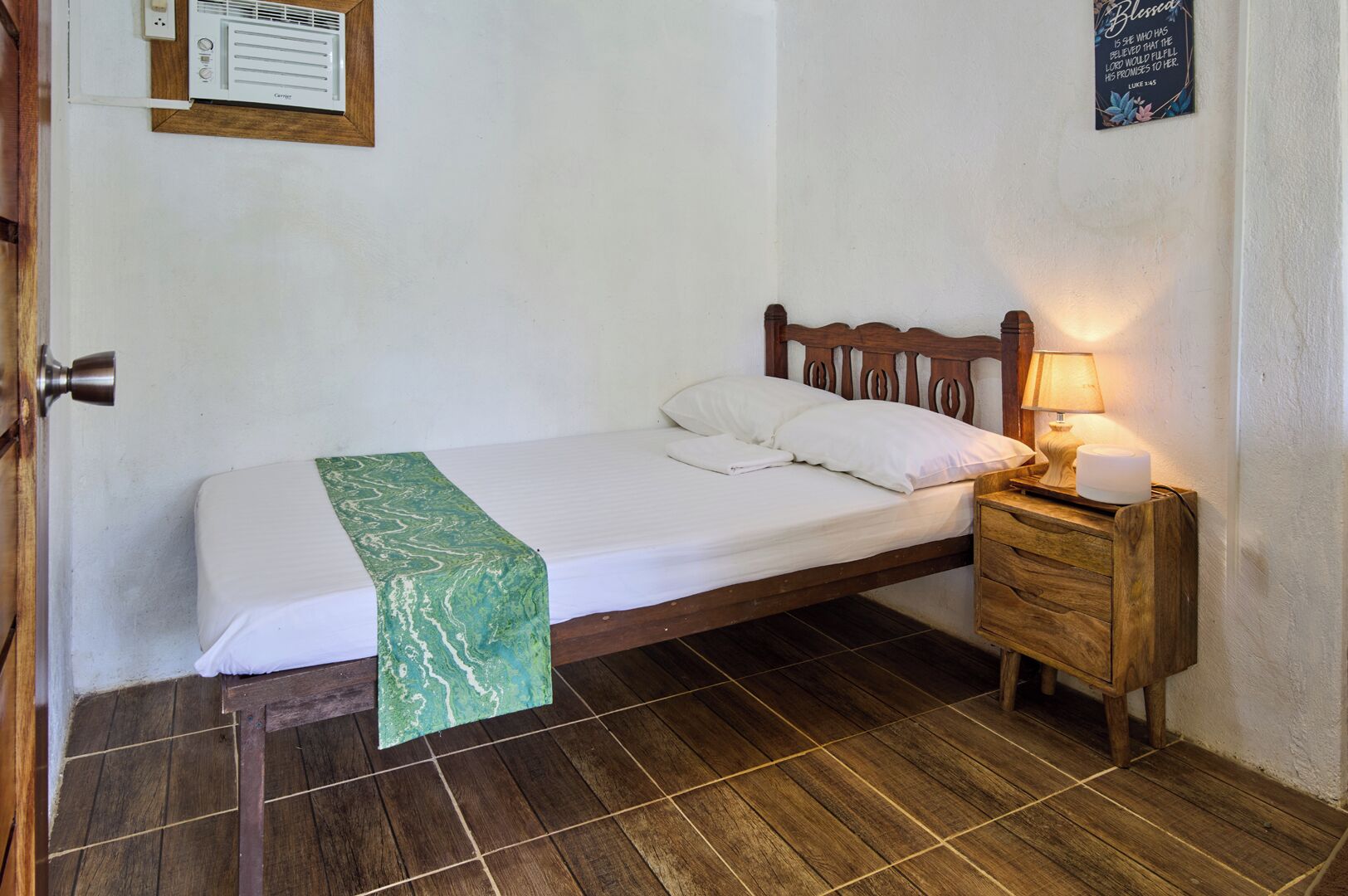 Una cama individual con cabecera de madera, una manta verde y una lámpara de noche.