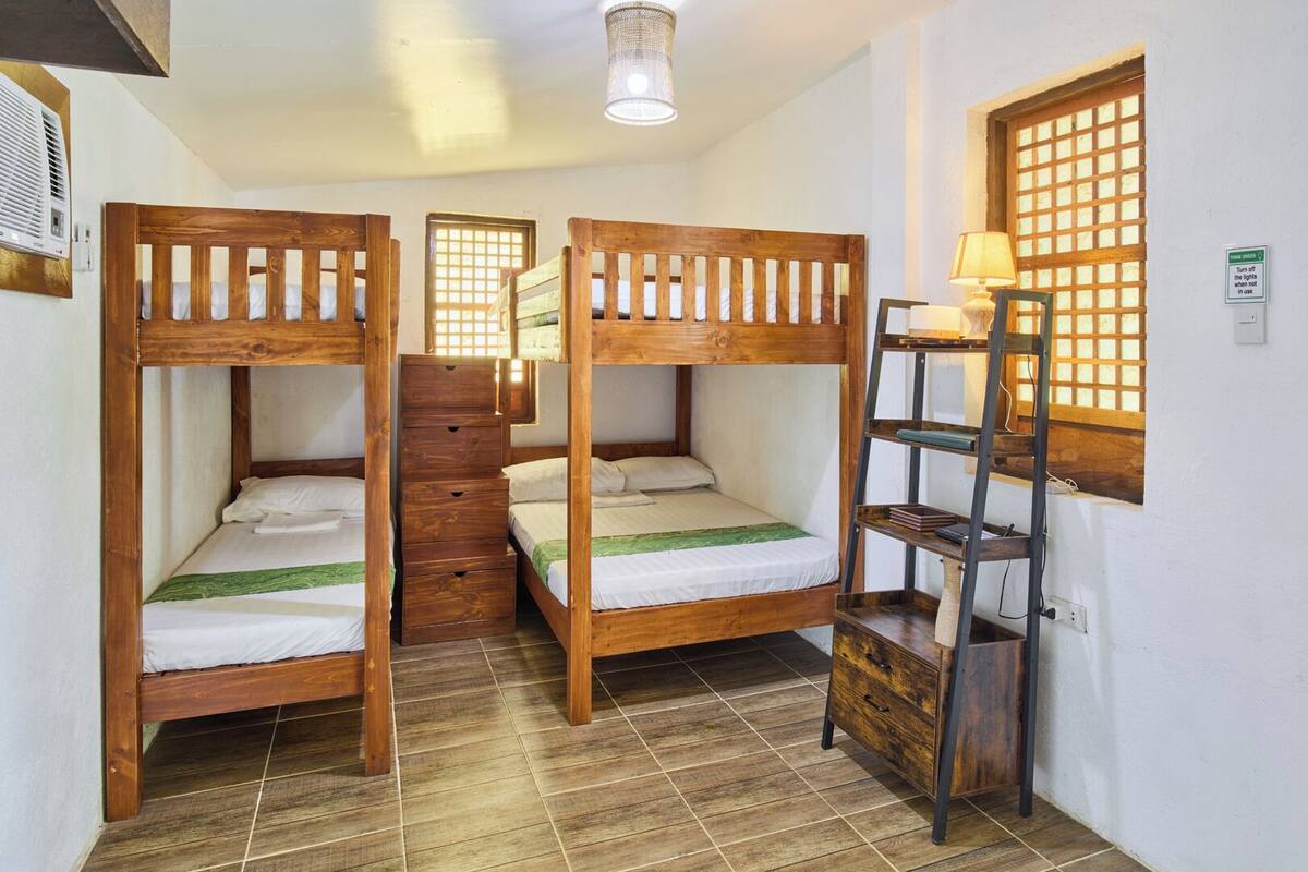 A dormitory room with bunk beds, a wooden ladder, a shelf, and a window with a grid pattern.