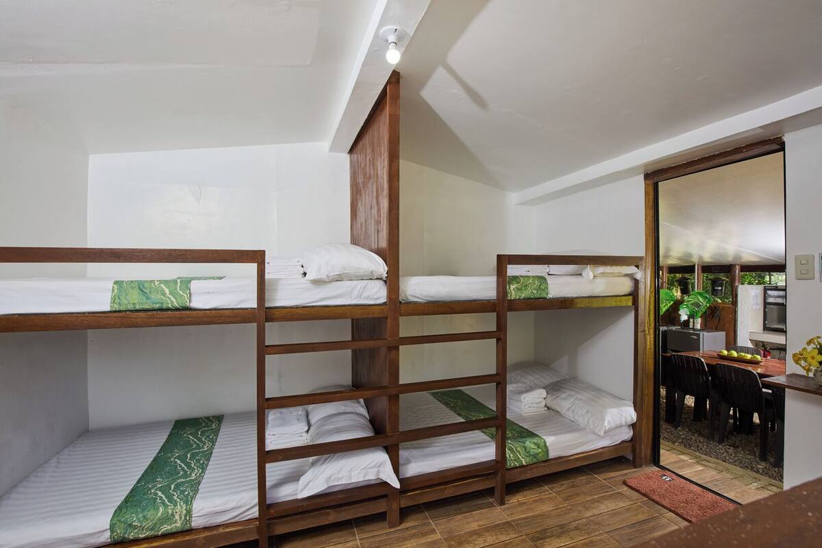 A dormitory room with bunk beds, a small kitchenette, and a view of the outside.