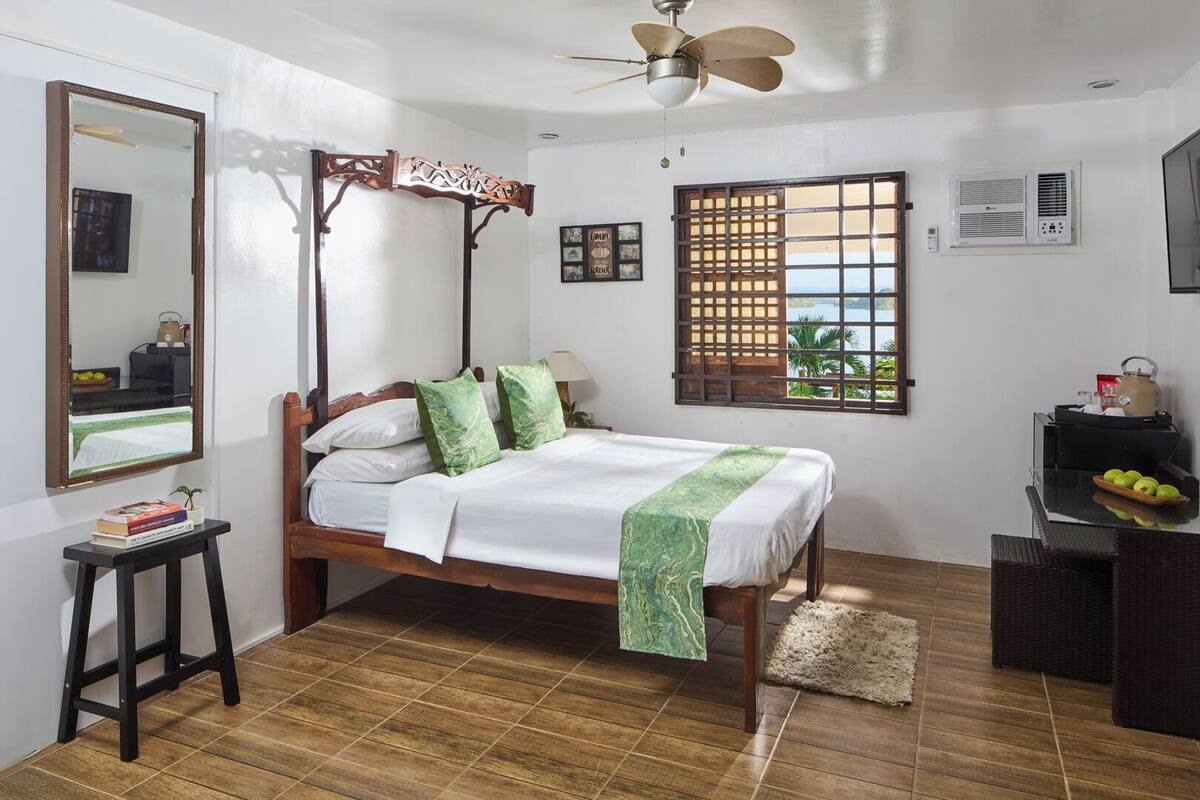 A neatly arranged bedroom with a wooden bed, a standing desk, a mirror, and a window with a view.