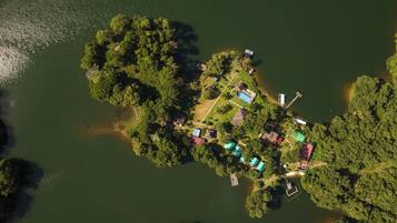 An aerial view of a small island with various buildings, including a swimming pool and multiple houses, surrounded by water.
