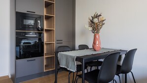Un coin repas comprenant une table, des chaises, un vase avec des fleurs séchées et un four encastré.