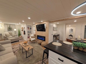 Una sala de estar moderna con un televisor de pantalla plana, un sofá, una mesa de centro y un comedor con una mesa de madera oscura.