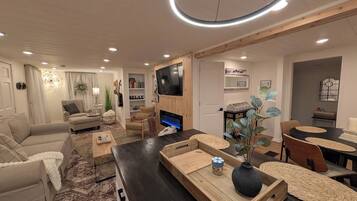 A modern living room with a flat-screen TV, a fireplace, and a dining area with a round table.