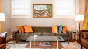 Una sala de estar con sofá, mesa de centro y un cuadro de un paisaje urbano.
