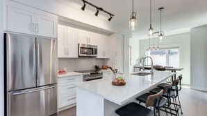 A modern kitchen with stainless steel appliances, white cabinetry, and a central island with bar stools. - Stunning Modern 2BR Unit in Downtown Canmore! (Canmore)