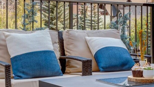 A balcony with a sofa and table, overlooking a mountainous landscape. - Stunning Modern 2BR Unit in Downtown Canmore! (Canmore)